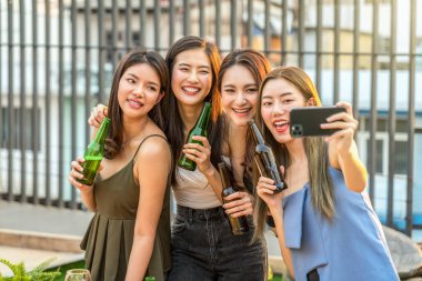 Mutlu Asyalı Kız Arkadaş Grubu 'nun çatıda gün batımında bira şişesi eşliğinde kutlama ve dans ederken selfie çekmesi, tavuk gecesi, tatil ya da yıllık parti konsepti.