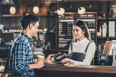 Asyalı müşteri temsilcisi cep telefonu bankacılığı başvurusu ile Asyalı küçük işletme sahibine küçük işletme sahibi ve kahve dükkânı sahibi olarak ödeme yapıyor.