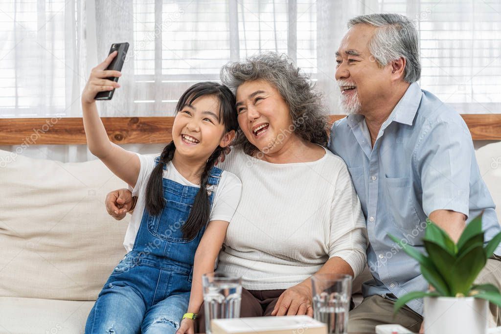 Asian Granddaughter taking selfie with  couple Grandparent with happy feeling by mobile phone in house, Long live and Elderly society, Warm family and happiness, leisure and lifestyle concept