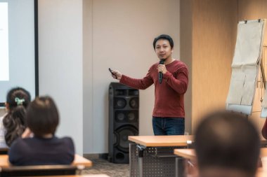 Asyalı konuşmacı, konferans salonu, seminer işi ve eğitim konseptini dinleyen seyircinin dikiz görüşü üzerinden sahnenin önünde bilgiyi gösteriyor ve sunuyor.