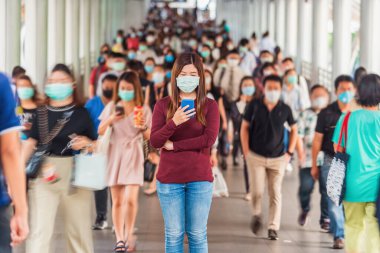 Bangkok taşımacılığında yoğun iş saatlerinde Coronavirus salgınını önlemek için tanınmayan iş adamları arasında cep telefonu kullanan Asyalı bir kadın.