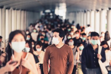 Bangkok taşımacılığında yoğun iş saatlerinde Coronavirus salgınını önlemek için cerrahi maske takan tanınmayan iş adamlarının arasında yürüyen Asyalı bir adam.