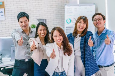 Asyalı iş adamlarından oluşan bir grup, modern işyerinde başparmak gösterip birlikte kameraya bakıyorlar, takım çalışması ve takım oluşturma, küçük işletme sahibi ve ortaklığı, onaylıyorlar ve kabul ediyorlar.