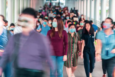 Bangkok taşımacılığında yoğun iş saatlerinde Coronavirus salgınını önlemek için cerrahi maske takan tanınmamış iş adamları kalabalığı arasında yürüyen Asyalı kadın.