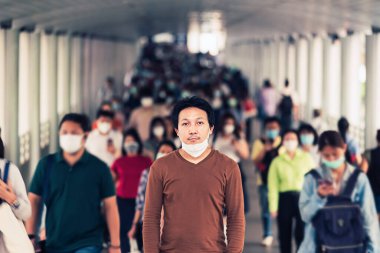 Bangkok taşımacılığında yoğun iş saatlerinde Coronavirus salgınını önlemek için cerrahi maske takan tanınmayan iş adamlarının arasında yürüyen Asyalı bir adam.