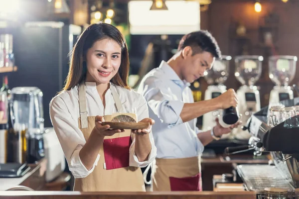 Asian Barista serving bakery cake, preparing cup of coffee, espresso with latte or cappuccino for customer order in coffee shop,Small business owner and startup in coffee shop and restaurant concept
