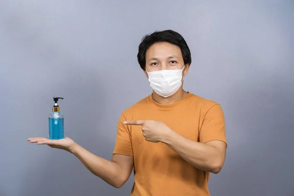 青い色の背景にアルコールジェルやハンドサニタイザーを指し 提示外科マスク顔を身に着けているアジアの男 Covid19発生とパンデミック 医療とウイルスの概念に対する保護 — ストック写真