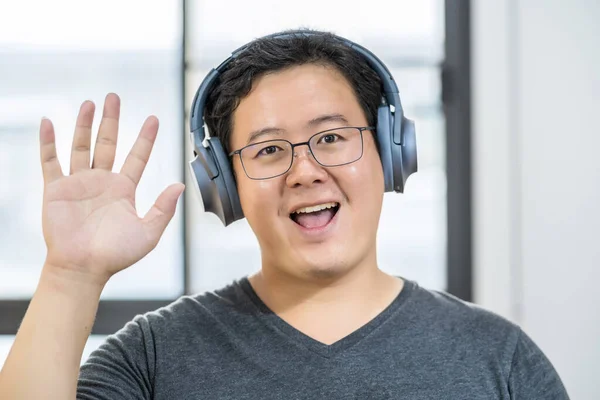 Asian business man waving hand for say hello when making video call to friend with social distancing, smiling female taking video blog recording vlog, Covid-19 pandemic, headphone and online meeting