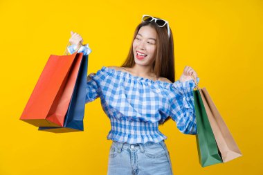 Çekici Asyalı gülümseyen genç kadın izole edilmiş sarı arka planda alışveriş çantaları taşıyor, fotokopi alanı ve stüdyo, siyah cuma sezonu satış konsepti.