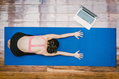 Top view Asian woman practicing yoga from home with laptop when Covid19 outbreak, healthy or Meditation Exercise, workout at home, coronavirus pandemic and quarantine, sports and healthcare in concept clipart