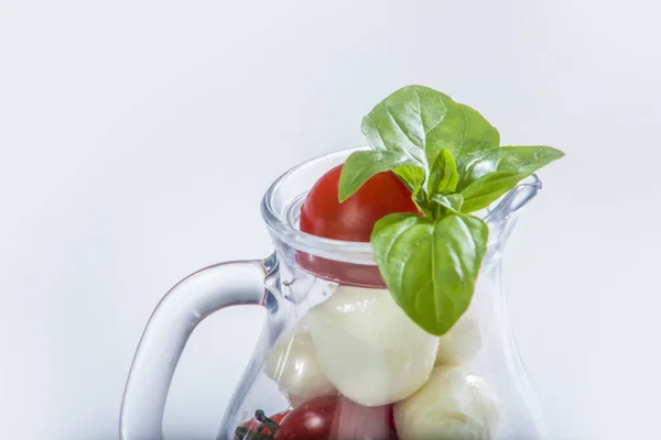 studio shot of basil leave on tomato in bowl with tomatoes and mozzarella inside