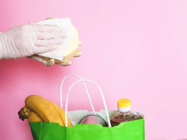 Yemek teslimatı. Ürünleri eve getirdikten sonra dezenfekte etmek. Elleri beyaz eldivenli, peçeteli..