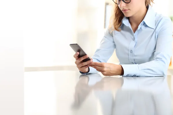 Mujer sentada en el escritorio con el teléfono celular en la mano — Foto de Stock
