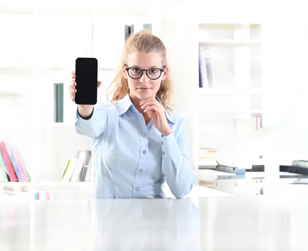 Woman showing mobile phone sitting at desk in office studio — Stock Photo, Image