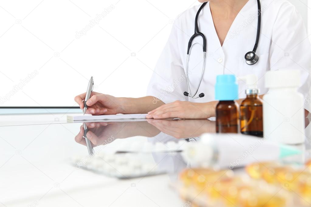 doctor writes the prescription in medical office with drugs on desk