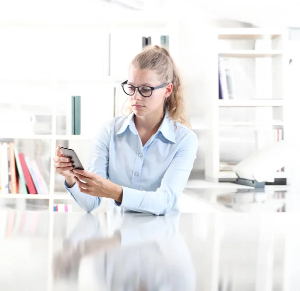 Mulher sentada na mesa com telefone celular na mão — Fotografia de Stock