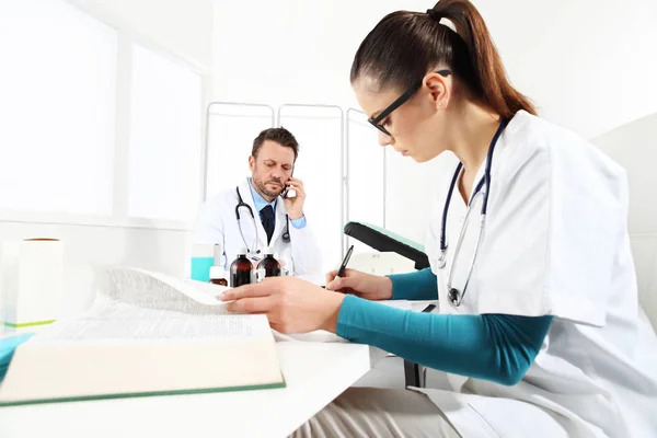 Doctor at mobile phone and nurse read text in medical office