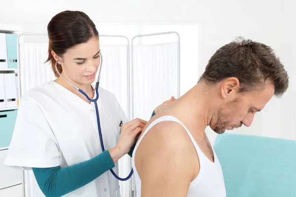 Doctor examining patient with stethoscope in medical office — Stock Photo, Image