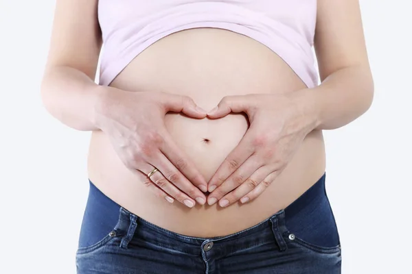 Gravid kvinna som håller händerna i hjärta form på magen, isolerade — Stockfoto