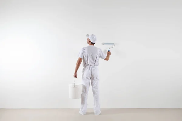 Vista trasera del pintor mirando a la pared en blanco, con rollos de pintura — Foto de Stock