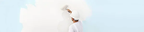 Rear view of painter man painting the wall, with paint roller, i — Stock Photo, Image