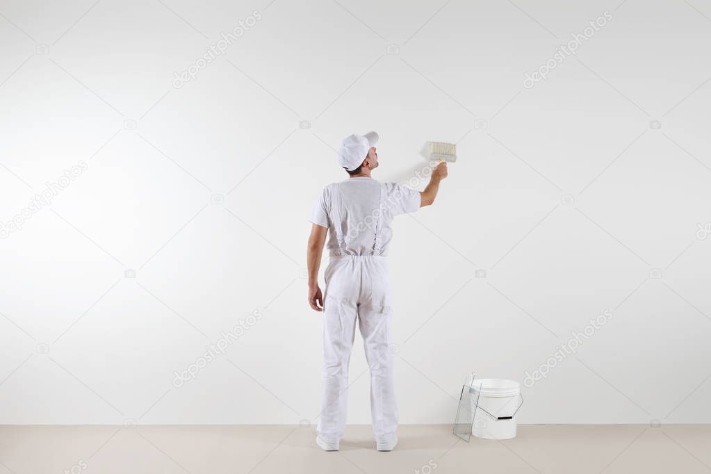 Rear view of painter man looking at blank wall, with paint brush