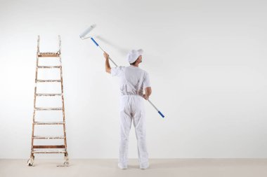 Silindir sopayla boş duvara bakarak ressam adam arkadan görünüş