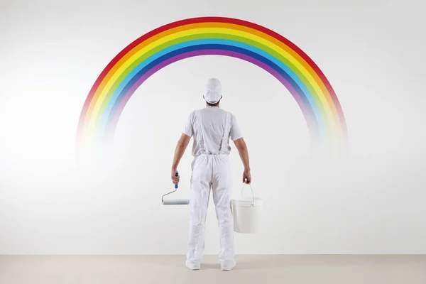 Vista trasera del pintor hombre mirando el arco iris en la pared en blanco — Foto de Stock