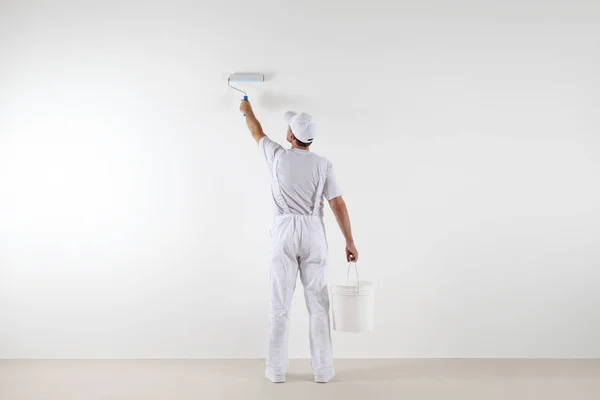 Visão traseira do pintor homem pintando a parede, com rolo de pintura — Fotografia de Stock