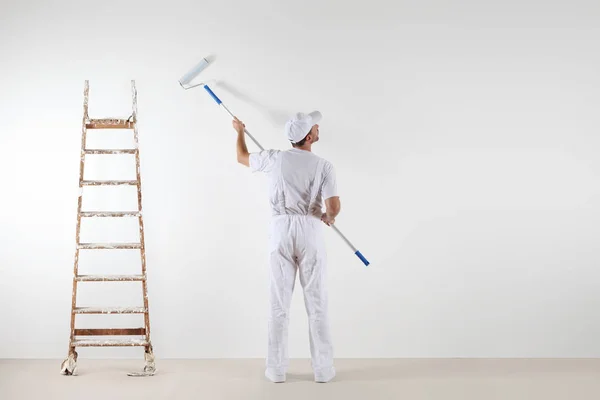 Achteraanzicht van schilder man kijken naar lege muur, met roller stok — Stockfoto