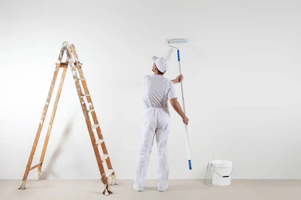 Visão traseira do homem pintor olhando para a parede em branco, com pau de rolo — Fotografia de Stock