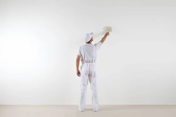 Vista trasera del hombre pintor mirando y pintando la pared en blanco — Foto de Stock