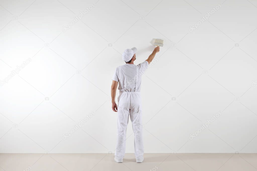 Rear view of painter man looking and painting blank wall