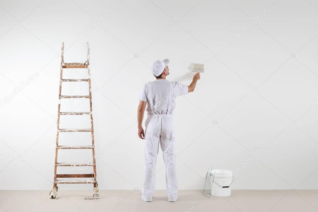 Rear view of painter man looking and painting blank wall