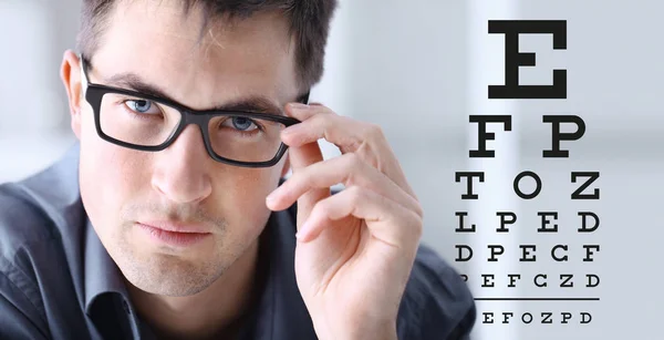 Cara masculina con gafas en el fondo de la tabla de prueba de la vista, el examen ocular concepto de oftalmología — Foto de Stock