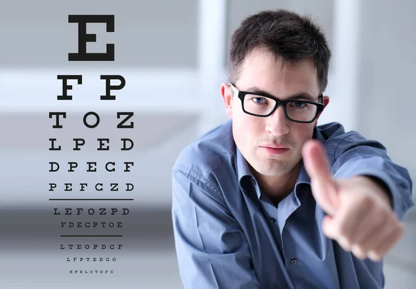 Manliga ansikte med glasögon på synförmåga testa diagrammets bakgrund, visar som hand, öga undersökning oftalmologi koncept — Stockfoto