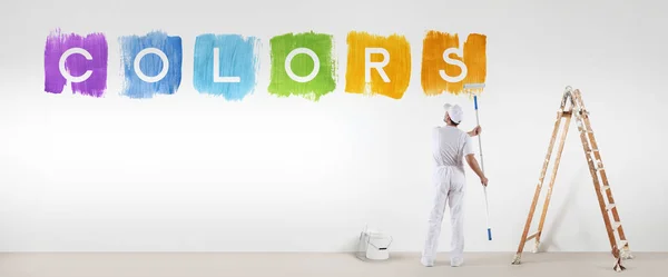 Painter man painting colors text isolated on blank white wall ba — Stock Photo, Image