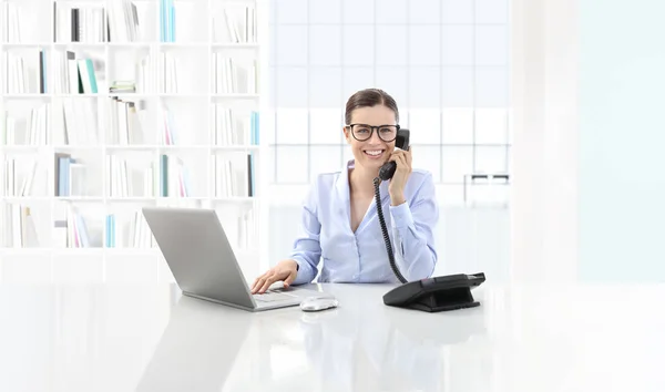 Lächelnde Frau im Büro telefoniert und benutzt den Computer — Stockfoto