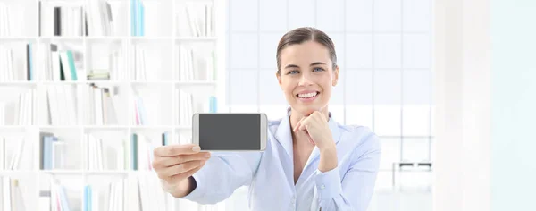 Mujer sonriente mostrando teléfono inteligente en su mano en la oficina interior — Foto de Stock