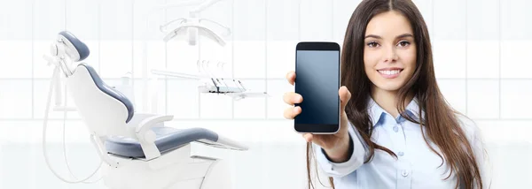Tandvård leende kvinna visar smarta telefonen på tandläkare klinik — Stockfoto