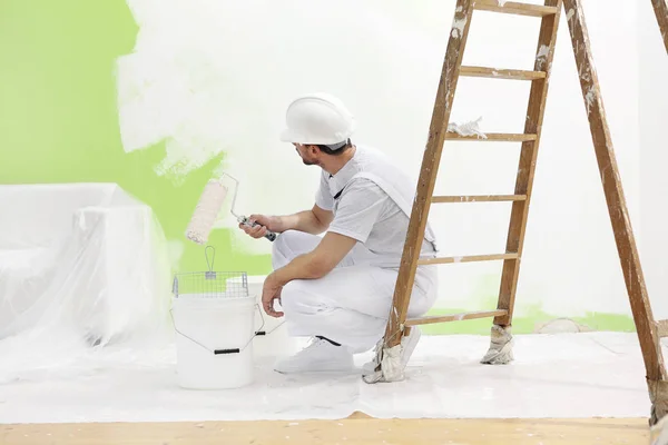 Painter man at work takes the color with paint roller from the b — Stock Photo, Image