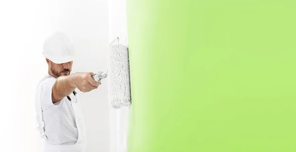 Pintor homem no trabalho com um rolo de pintura, pintura de parede col verde — Fotografia de Stock