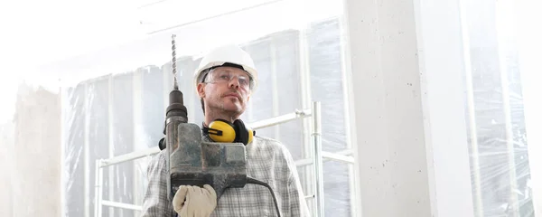 Mann Mit Elektrobohrmaschine Professioneller Bauarbeiter Mit Schutzhelm Kopfhörer Handschuhe Und — Stockfoto