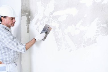 İç inşaat alanının duvarını alçılayan alçıcı adam miğfer ve koruyucu eldiven takıyor, izole edilmiş beyaz duvardaki boşluğu kopyalayıp kopyalıyor.