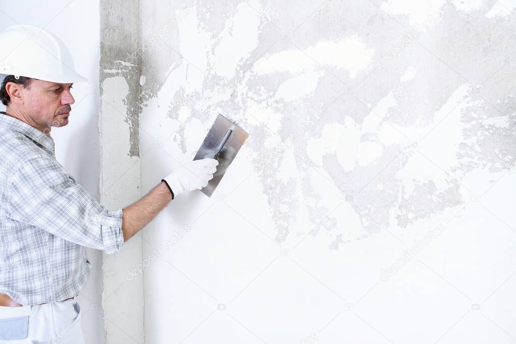 plasterer man at work with trowel plastering the wall of interior construction site wear helmet and protective gloves, isolated and copy space on white wall