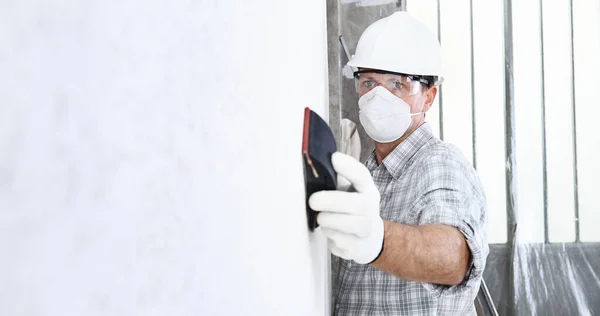 Mann Schmirgelt Wand Mit Schleifpapier Bauarbeiter Mit Maske Schutzhelm Handschuhen — Stockfoto