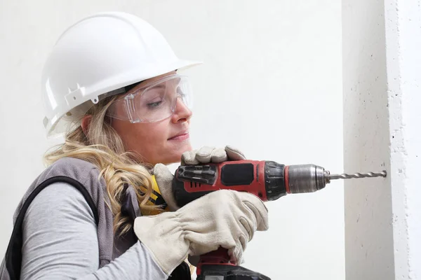 女合同工使用无绳钻机在墙上打洞 建筑工人戴安全帽 戴耳机 戴手套和防护眼镜 合上肖像 — 图库照片