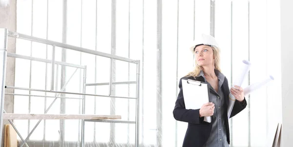 女建筑师或建筑工程师戴着头盔 在有窗户和脚手架的建筑工地内拿着文件夹和蓝图 背景是全景图像 — 图库照片