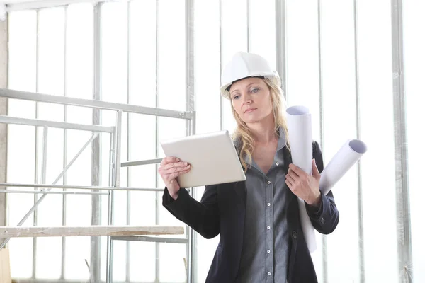 女性建筑师或建筑工程师 戴着数码平板头盔 在有窗户和脚手架的建筑工地内持有图纸 — 图库照片