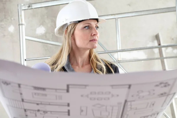在以脚手架为背景的建筑工地内 女建筑师或建筑工程师在阅读设计图时都戴着头盔 — 图库照片